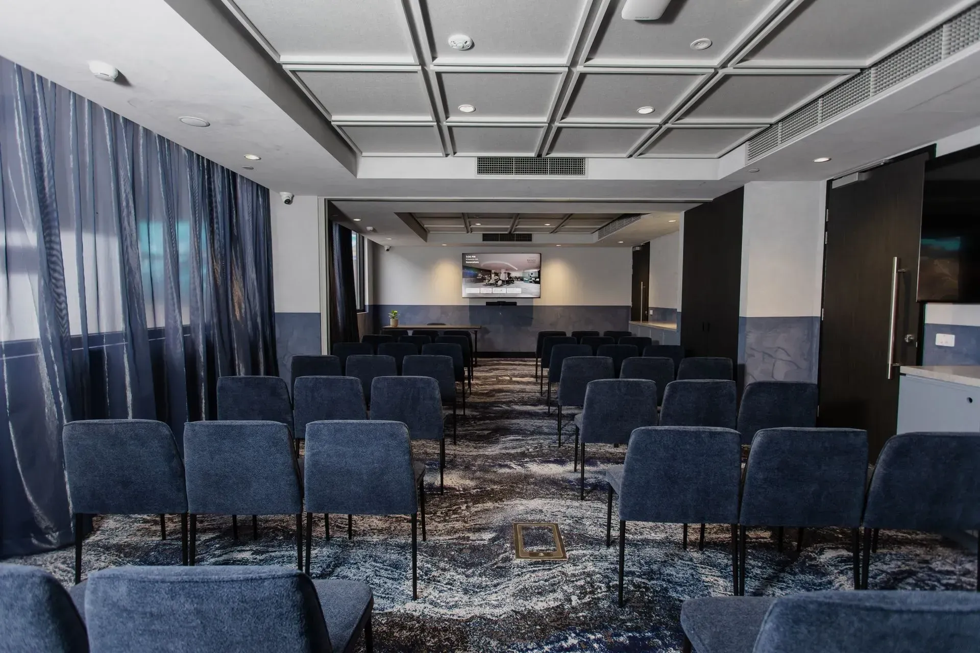 Empty conference room with rows of dark blue chairs facing a front screen and stage
