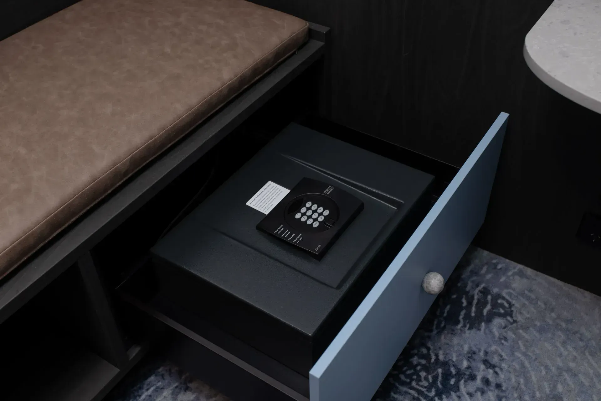 Open drawer with a black keypad and white card beside a bed.