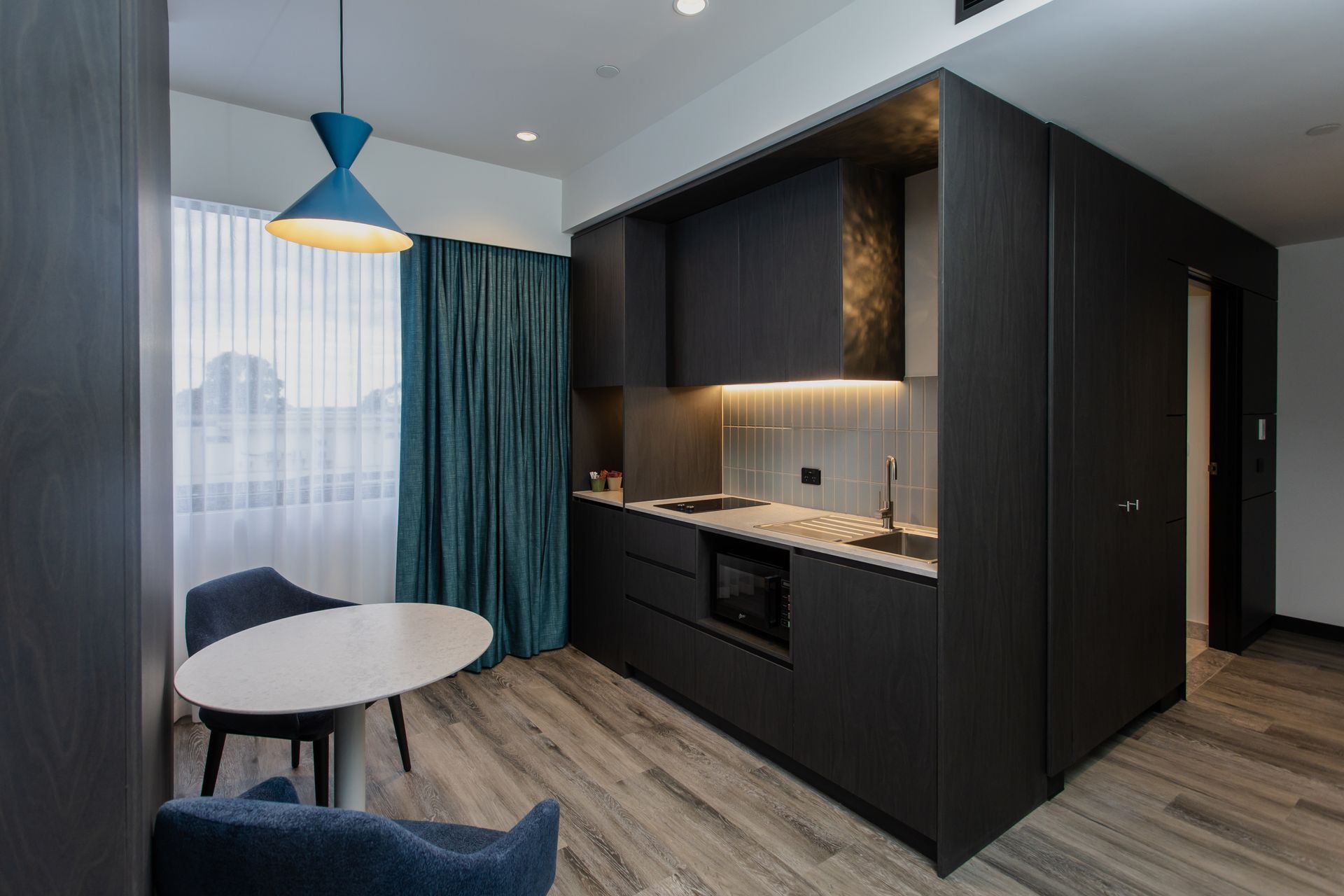 Modern studio apartment with kitchenette, round table, blue curtains.