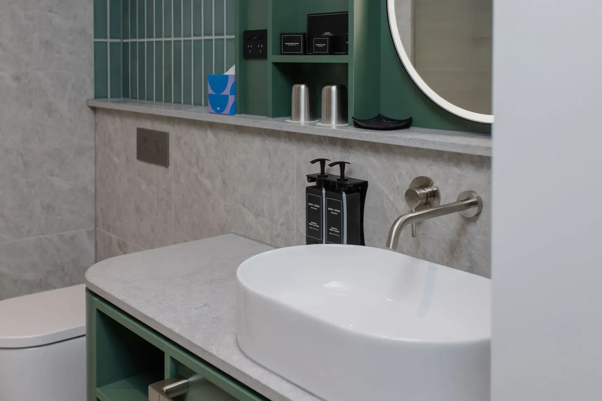 Modern bathroom vanity with white sink, green shelving, mirror, and tiled walls