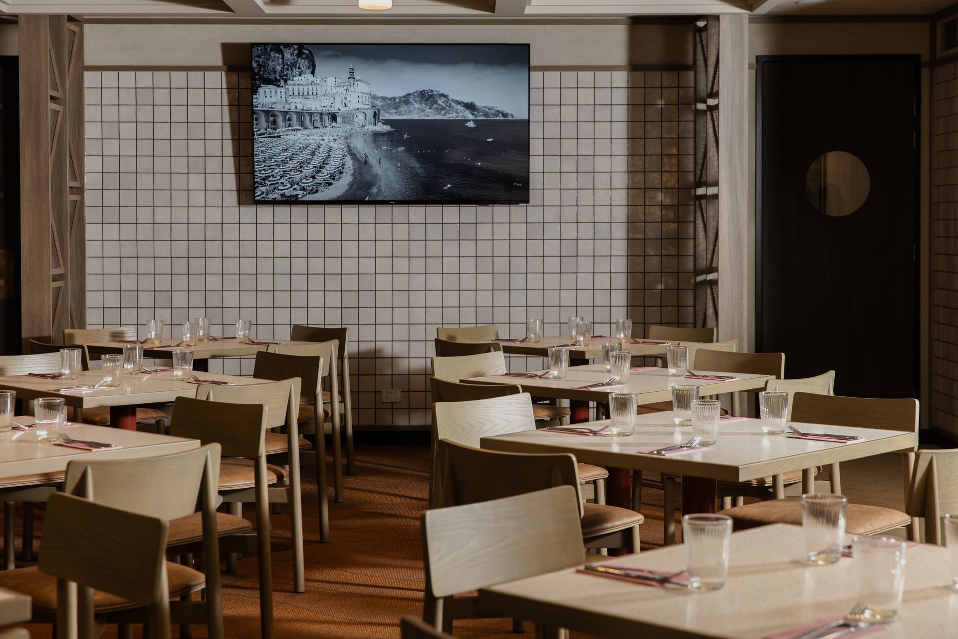 Empty modern dining room with neatly set tables and a wall-mounted TV showing an Italian landscape