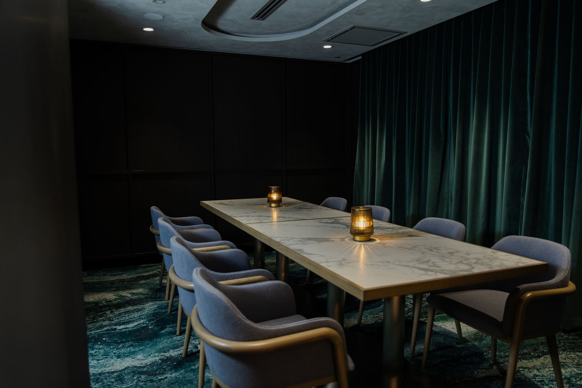 Dim private dining room with a long marble table, blue chairs, candles, and dark curtains