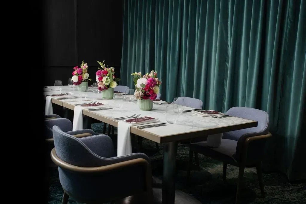 Elegant dining table set with floral centerpieces beside green curtains in a dim room