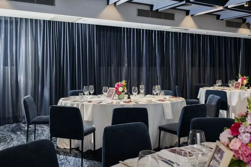 Elegant banquet hall with round tables, black chairs, and dark floor-to-ceiling curtains