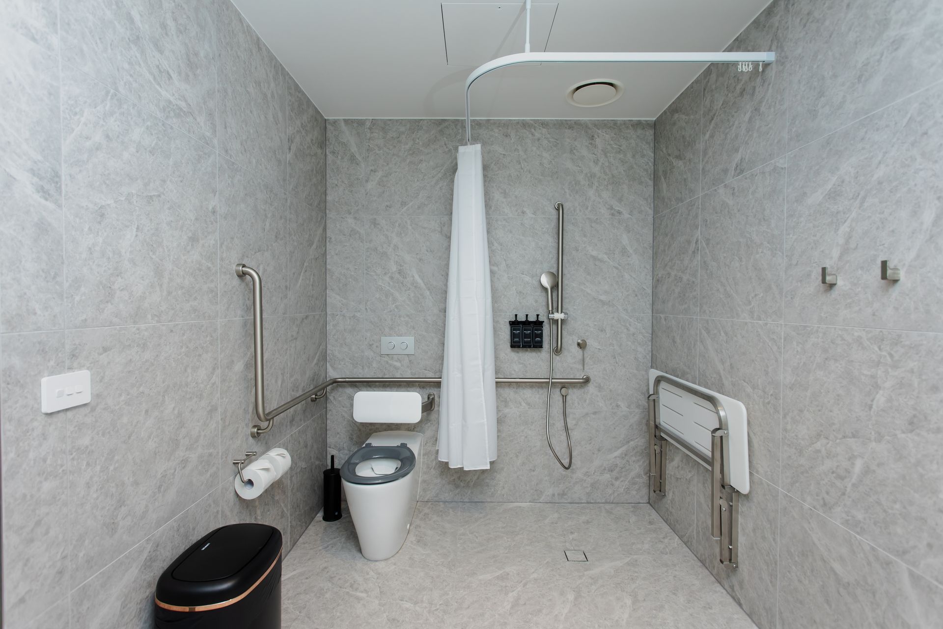 Accessible bathroom with toilet, shower, grab bars, and a wall-mounted sink in a tiled room