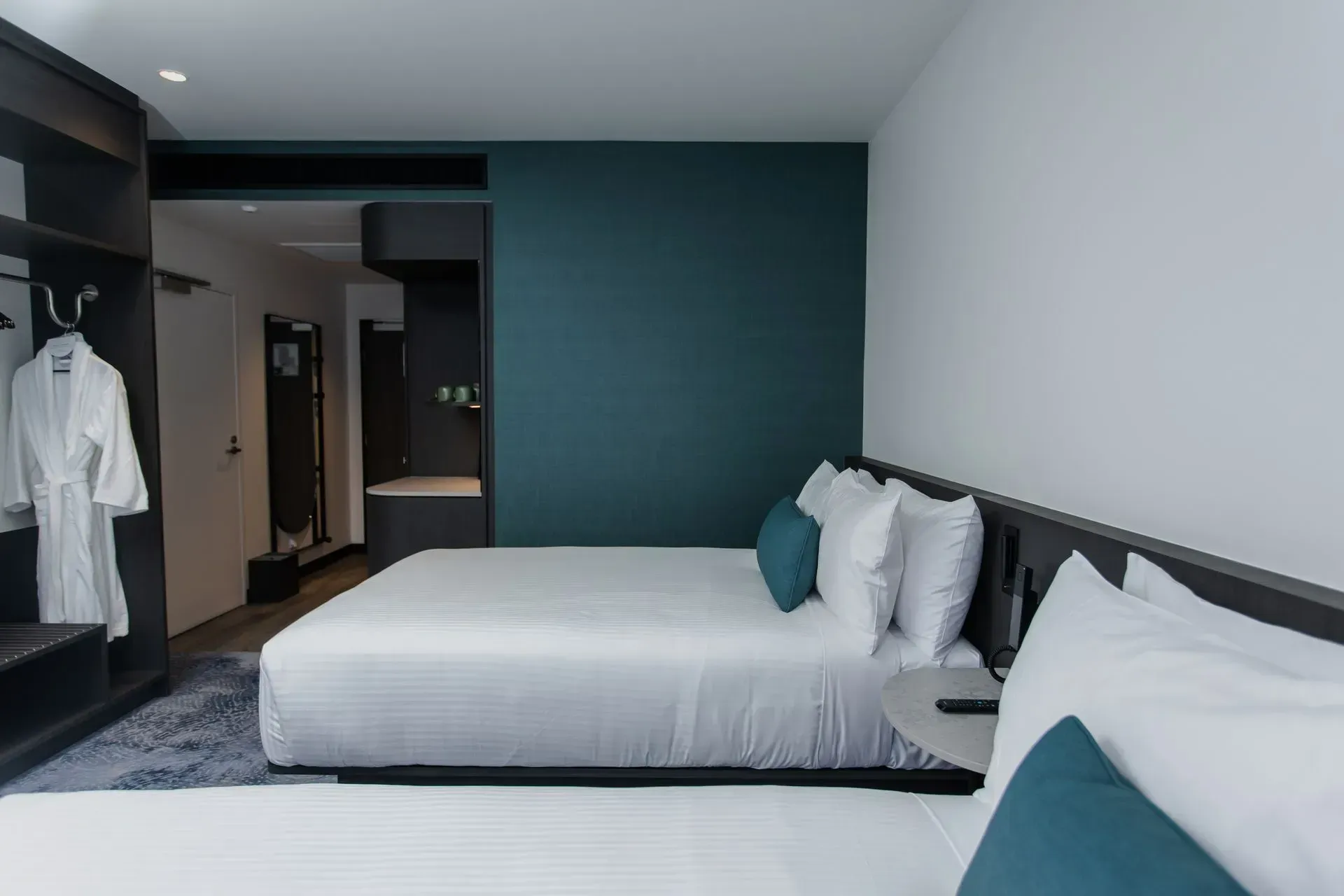 Modern hotel room with two white beds, dark teal accent wall, and an open closet area