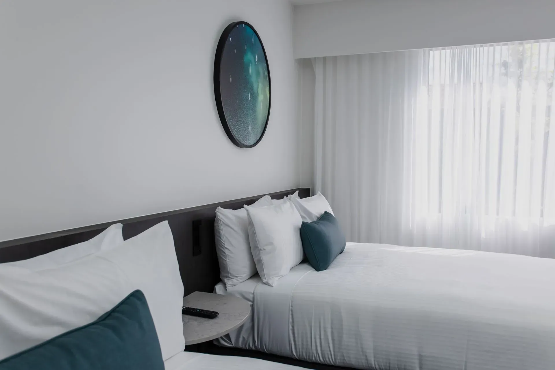 Modern bedroom with two twin beds, teal pillows, wall art, and sheer curtains by a bright window