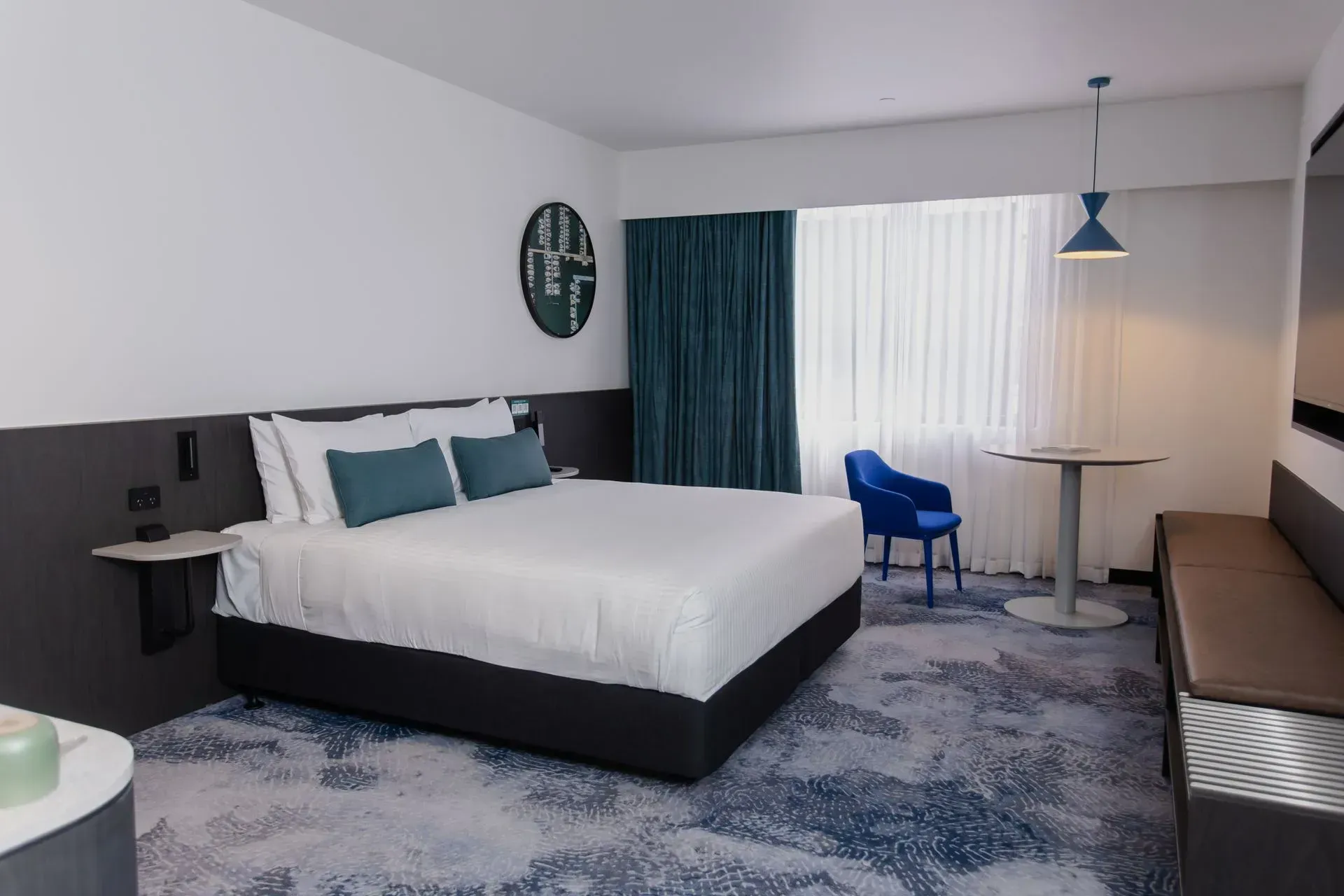 Modern hotel room with a king bed, blue chair, desk, and window curtains