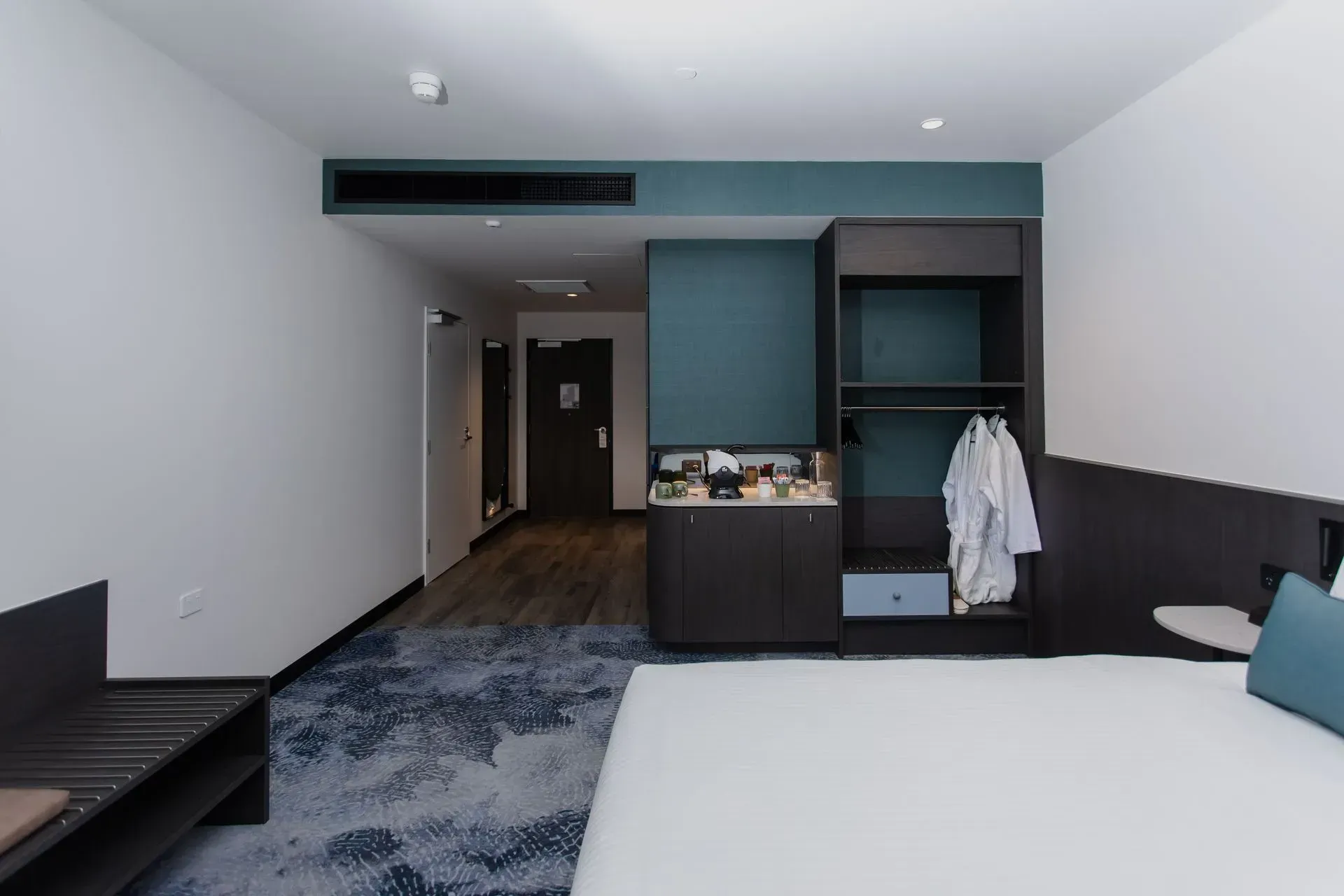 Modern hotel room with two beds, teal accents, wood floor, and open closet area