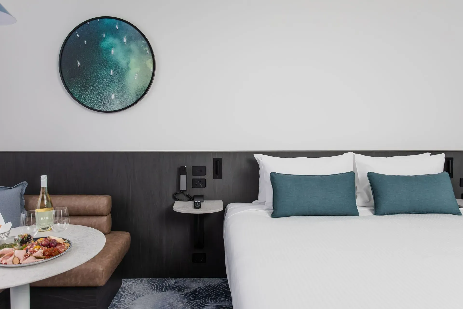 Hotel room with bed, teal pillows, bedside table, and breakfast tray on a bench