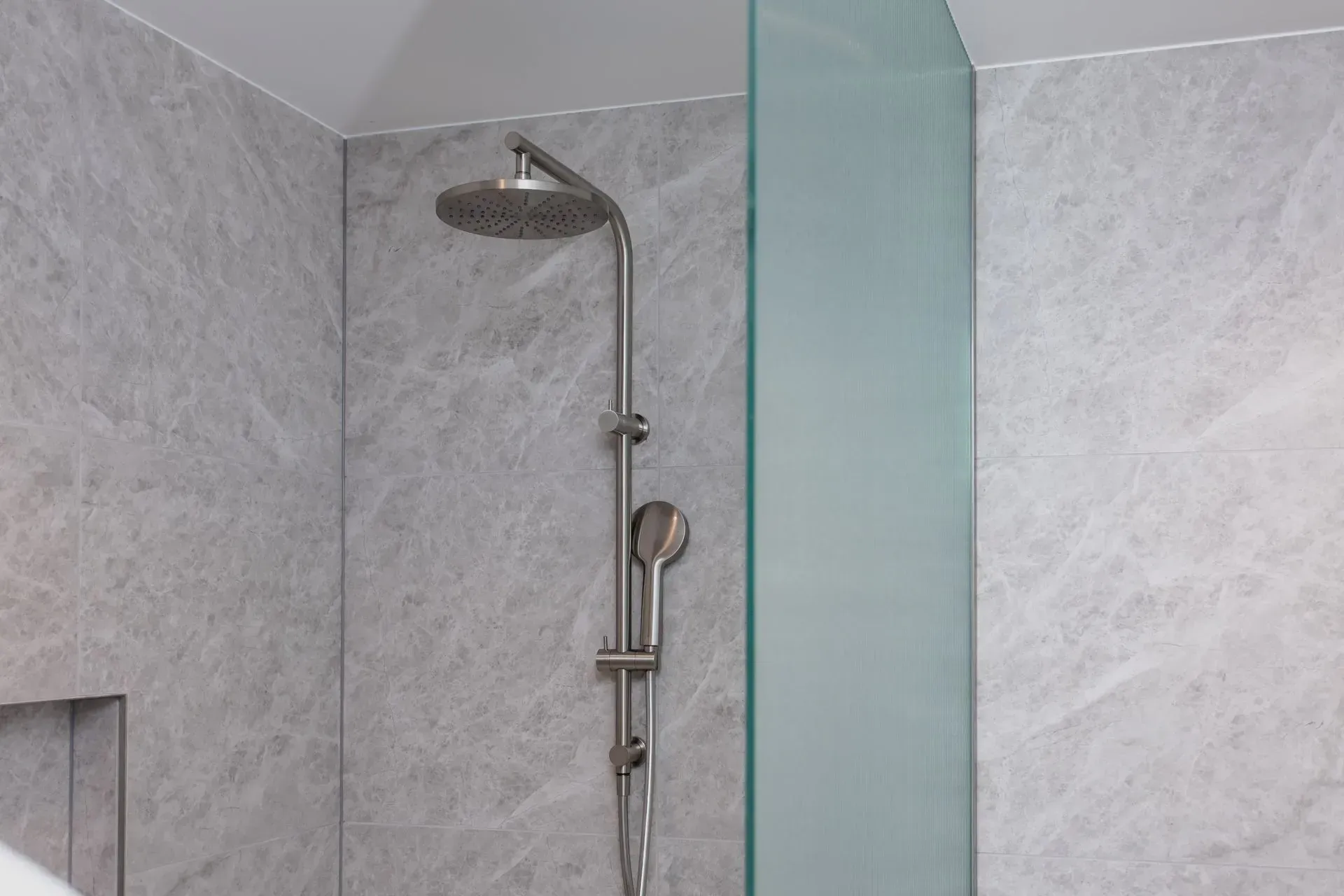 Modern tiled shower with chrome showerhead and frosted glass partition