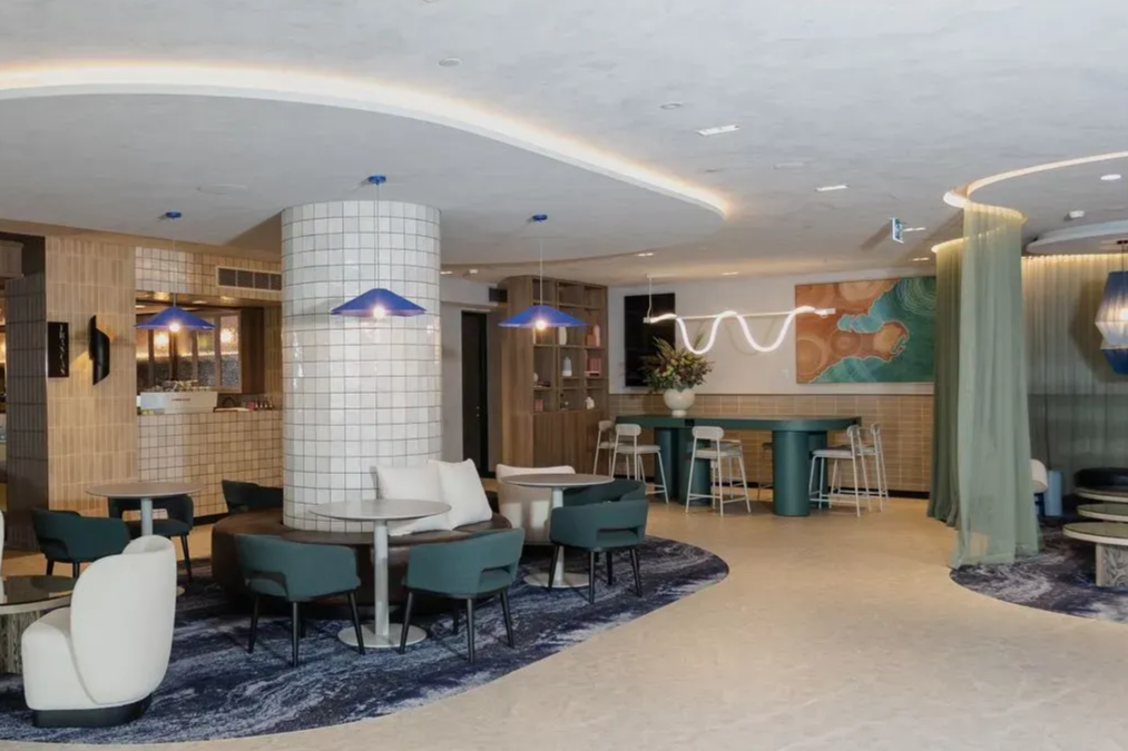 Modern lounge with curved seating, teal chairs, and abstract wall art in a softly lit interior.