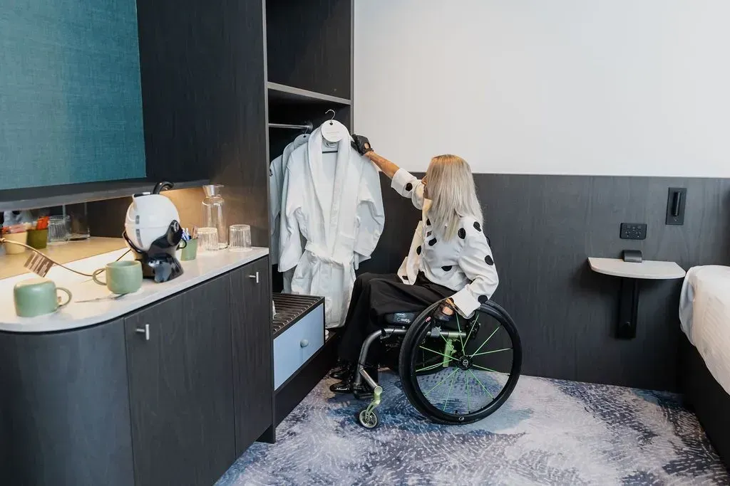 Person in a wheelchair reaching for clothes in a closet inside a modern room.