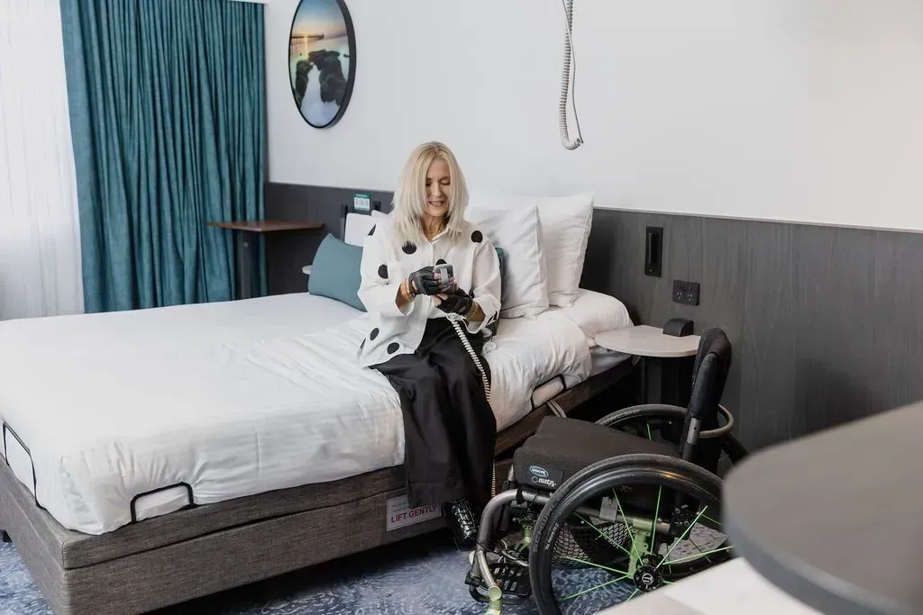 Person sitting on a bed in a modern bedroom, with a wheelchair in the foreground.