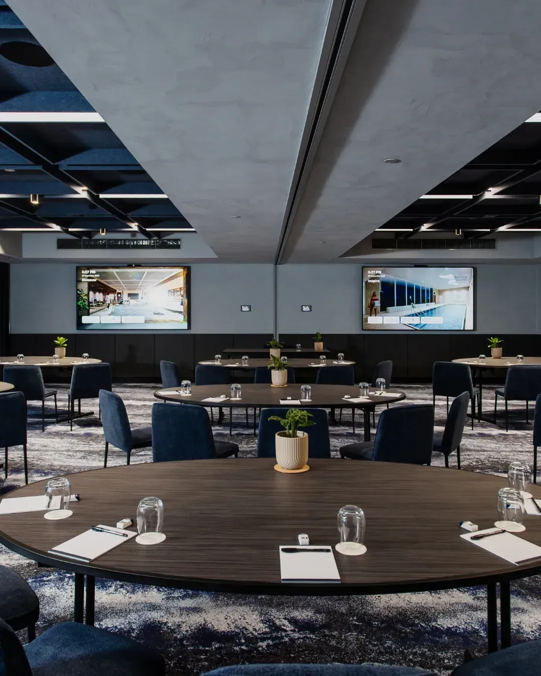 Modern restaurant dining room with round tables, blue chairs, and geometric ceiling panels