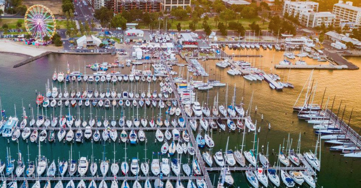 Aerial view of a marina packed with boats beside a waterfront fairground with a Ferris wheel at sunset