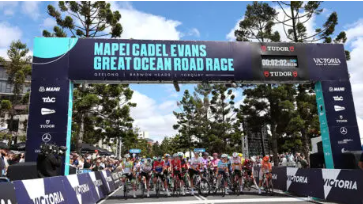 Cyclists start the Mapei Cadel Evans Great Ocean Road Race under a blue arch on a tree-lined street