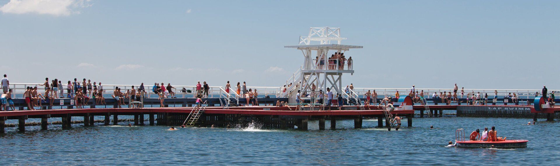 Crowded pier over blue water with a white diving tower