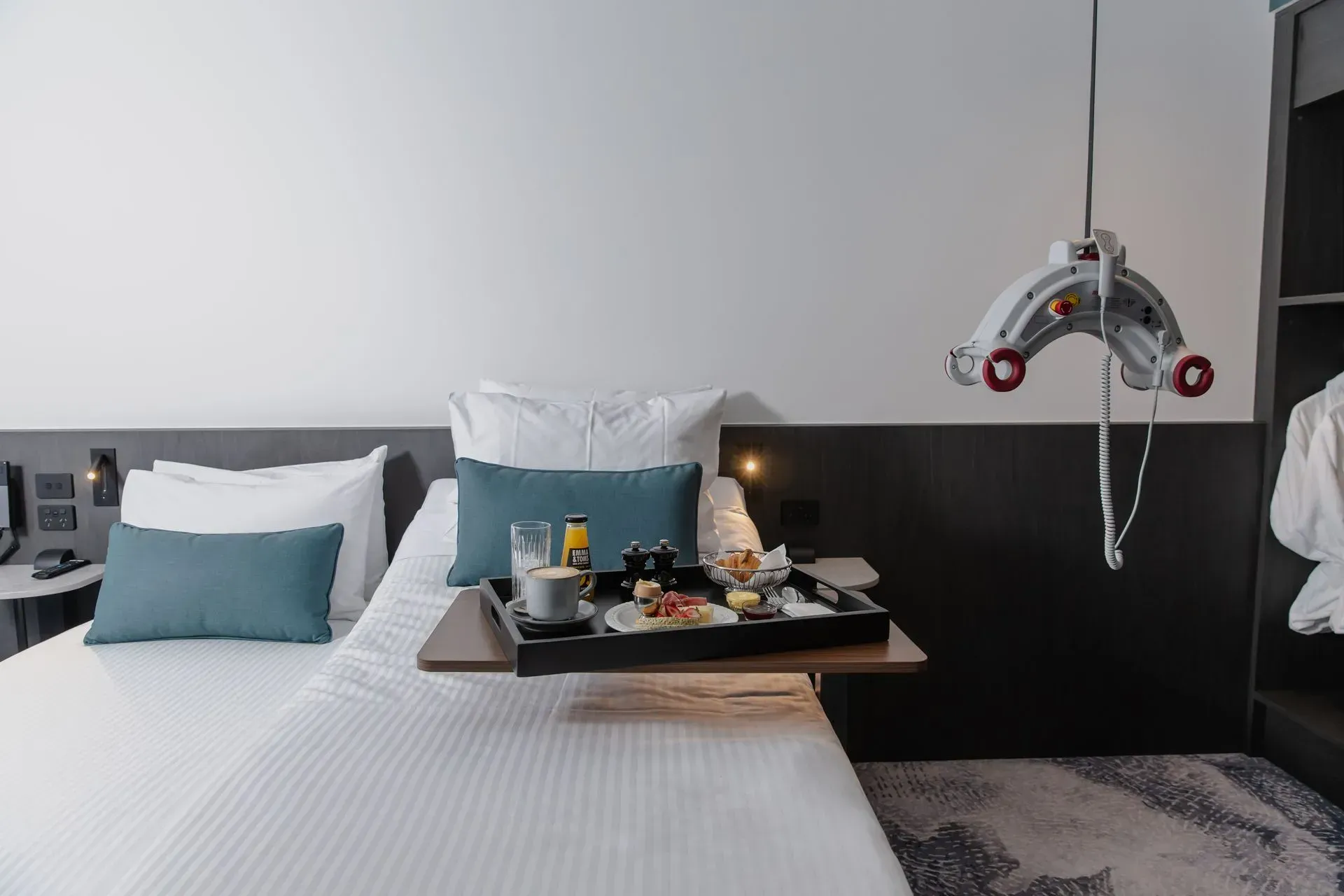 Hotel room with twin beds, breakfast tray, and an assist lift hanging near the wall