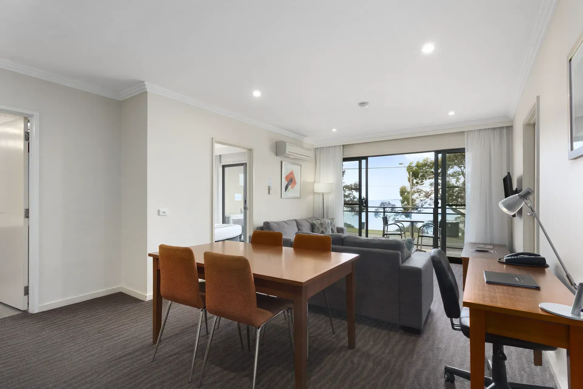 Modern open-plan living room with dining table, gray sofa, and large windows overlooking water