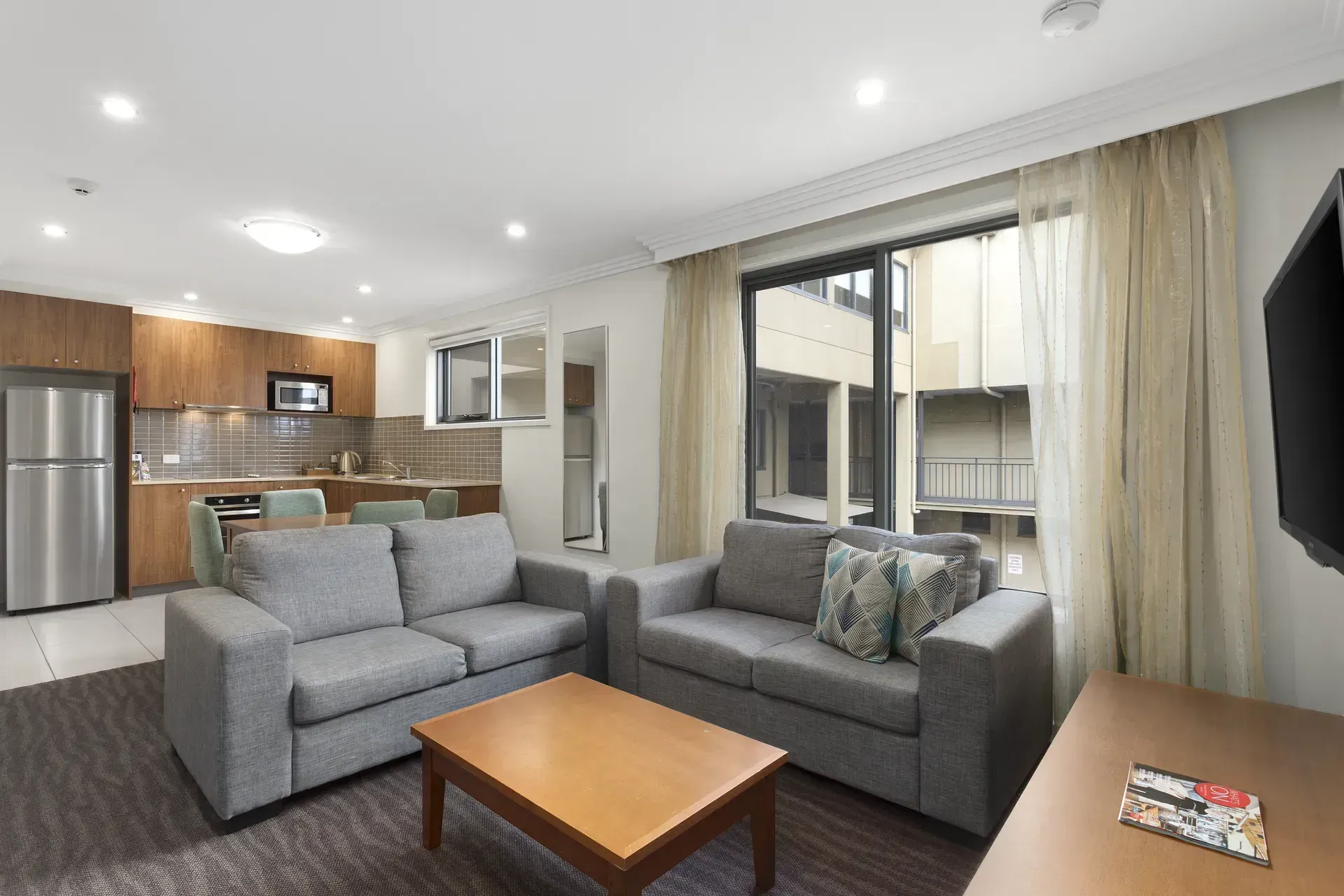 Modern living room with gray sofas, coffee table, and open kitchen with stainless appliances