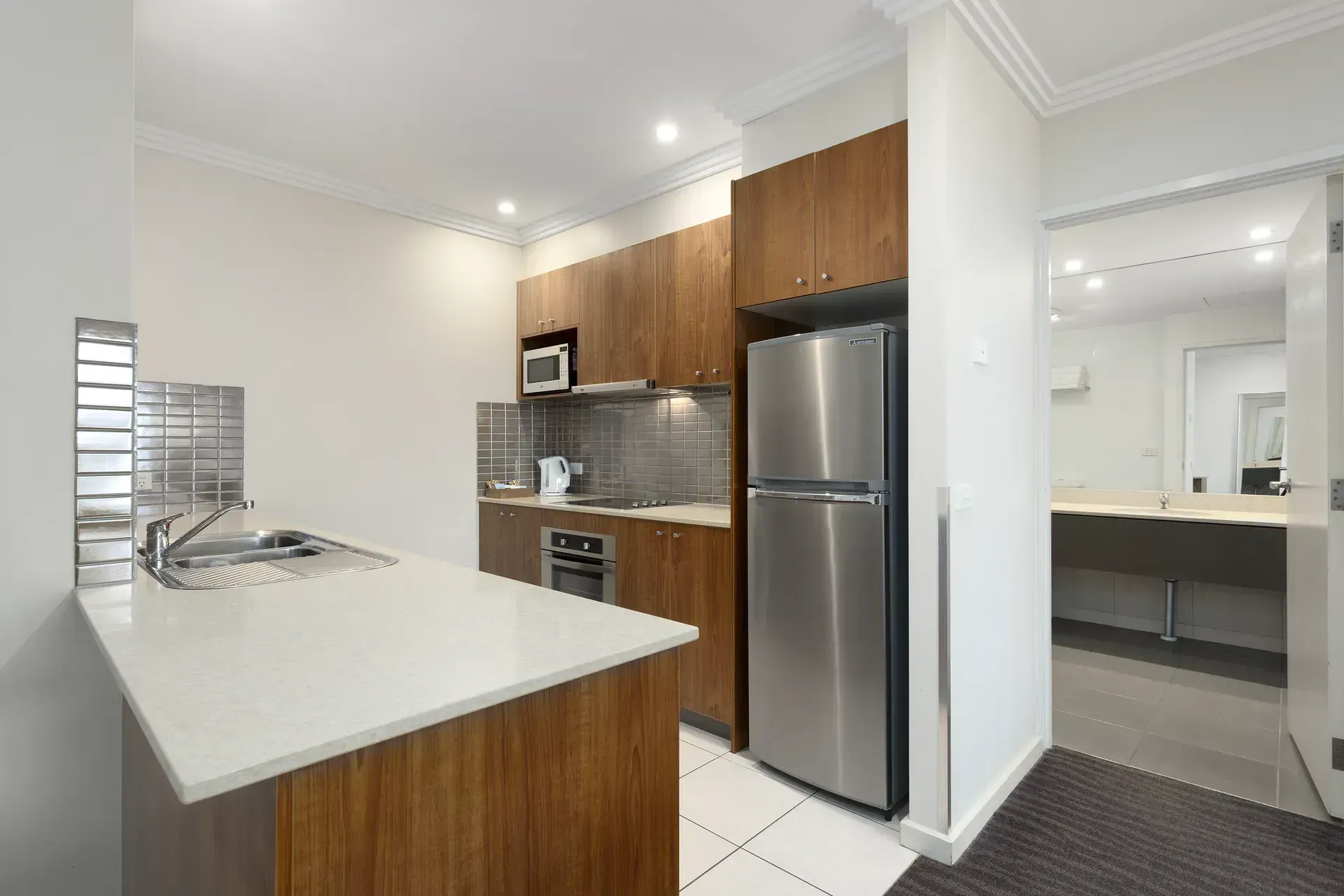 Modern kitchen with white island, wood cabinets, stainless-steel fridge, and bright open-plan layout
