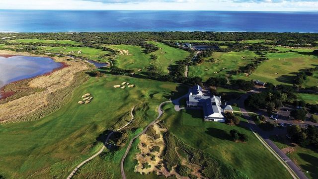 Aerial view of a coastal golf course with green fairways, water, and a house near the shoreline