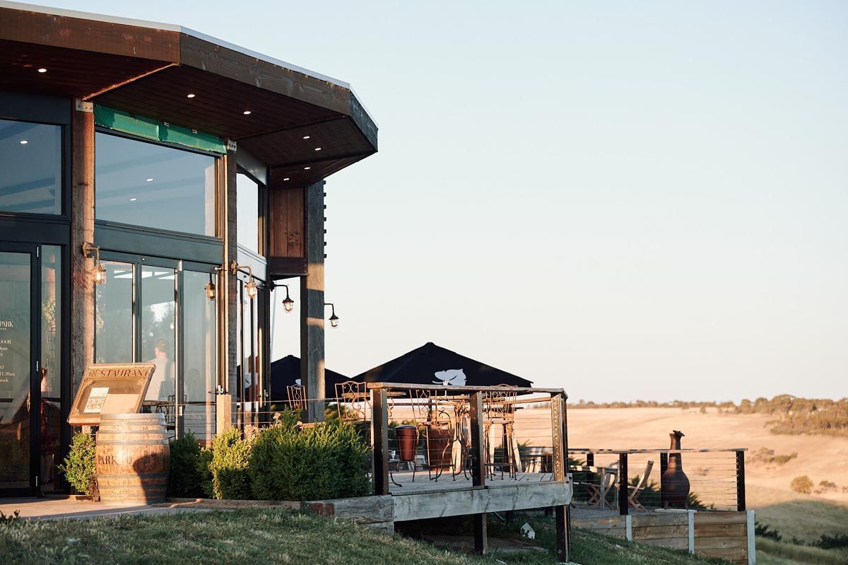 Modern glass winery building with wooden deck overlooking a wide open field at sunset
