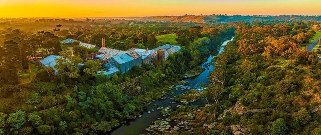 Aerial view of a lush green valley with a river, buildings, and golden sunset light