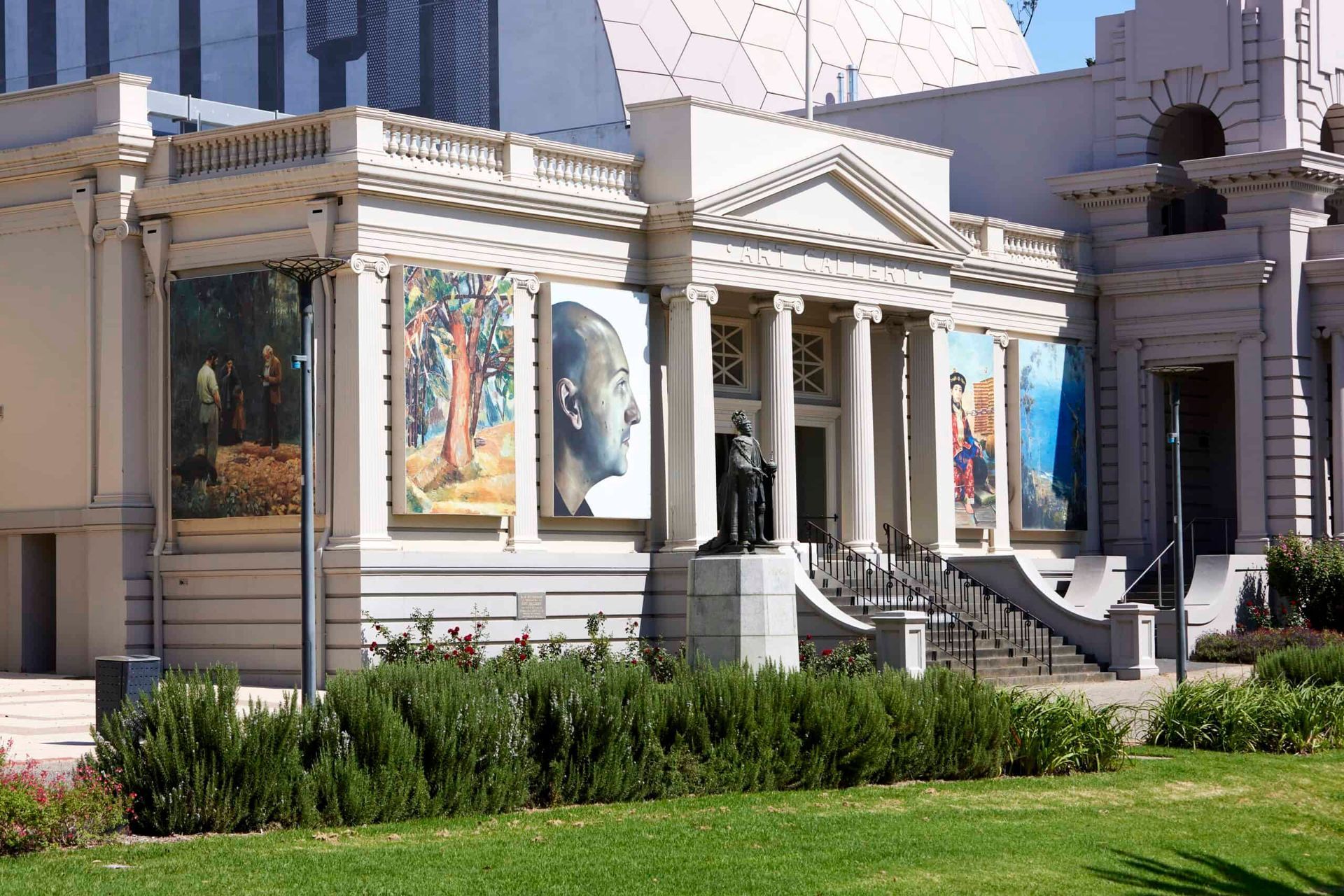Museum facade with classical columns, large banners, and a green lawn in front