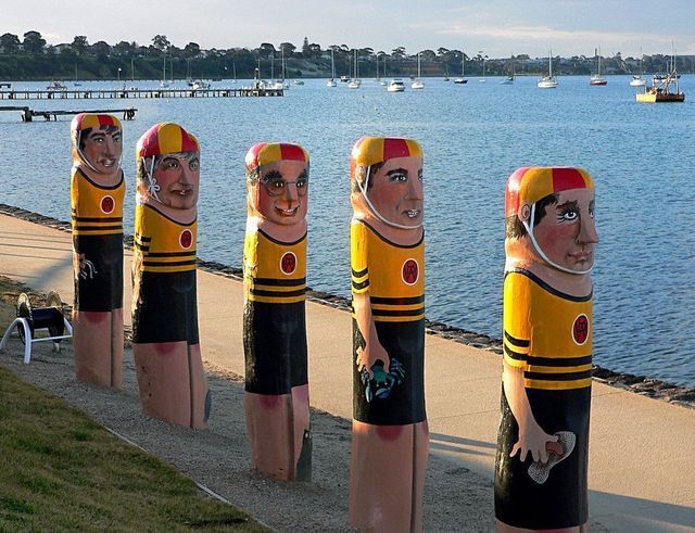 Five painted wooden bollards on a bayside path, with boats and water in the background