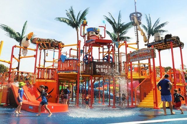 Colorful water playground with slides, palm trees, and children splashing on a sunny day