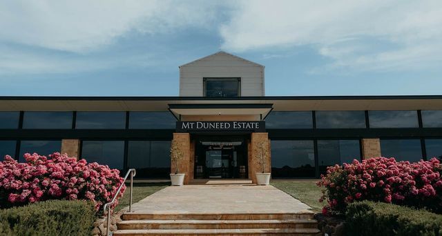 Front entrance of Mt. Dunned Estate with steps, glass doors, and pink flowering bushes on both sides