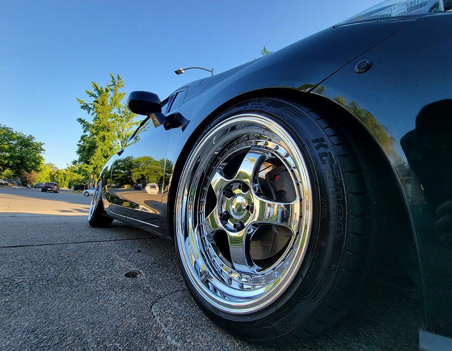 A black car with chrome wheels and tires is parked on the side of the road