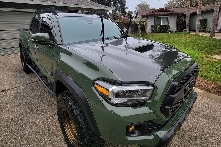 A green toyota tacoma truck is parked in front of a house.