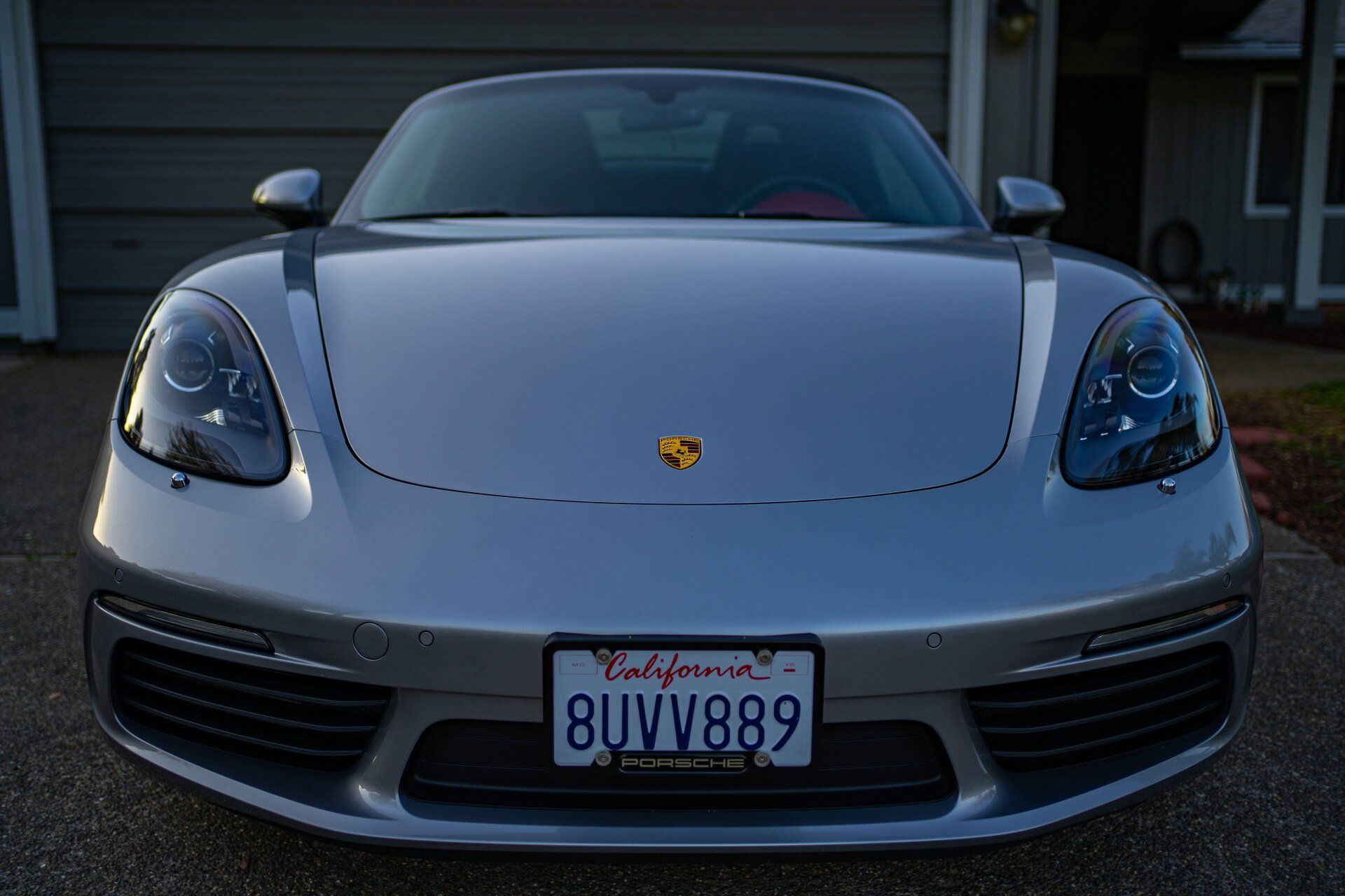A silver sports car with a california license plate is parked in front of a garage.