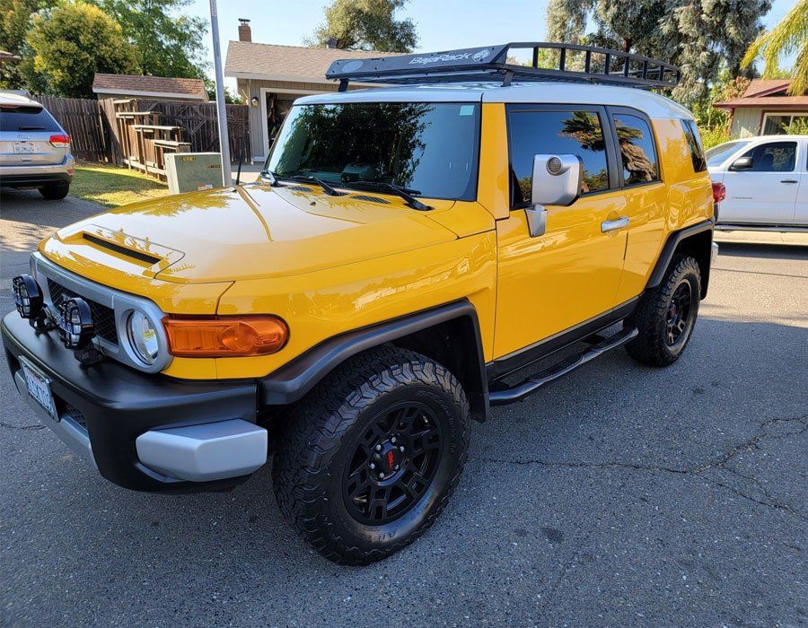 A yellow toyota fj cruiser is parked in a parking lot.