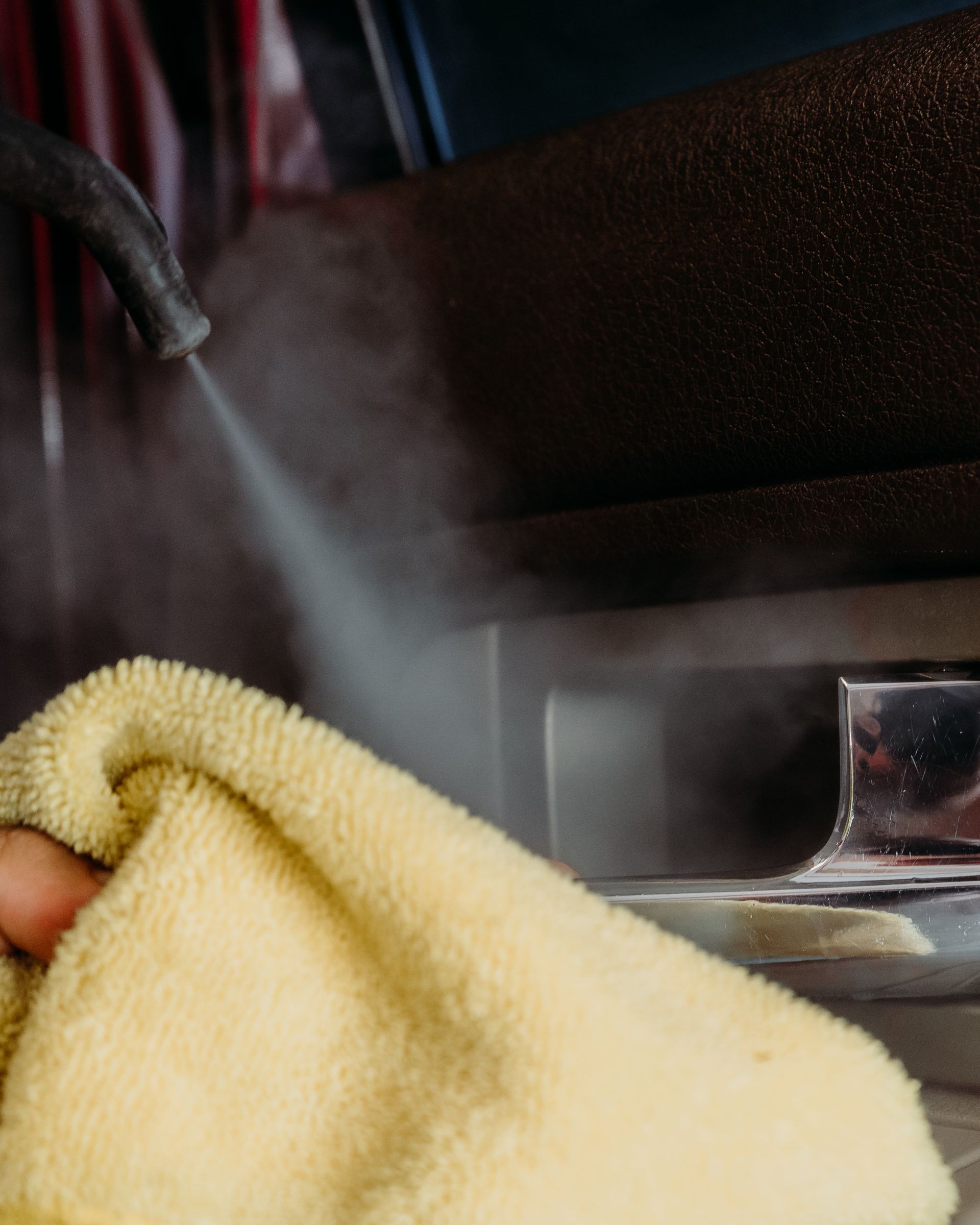 A person is cleaning a stove with a towel and steam coming out of it.