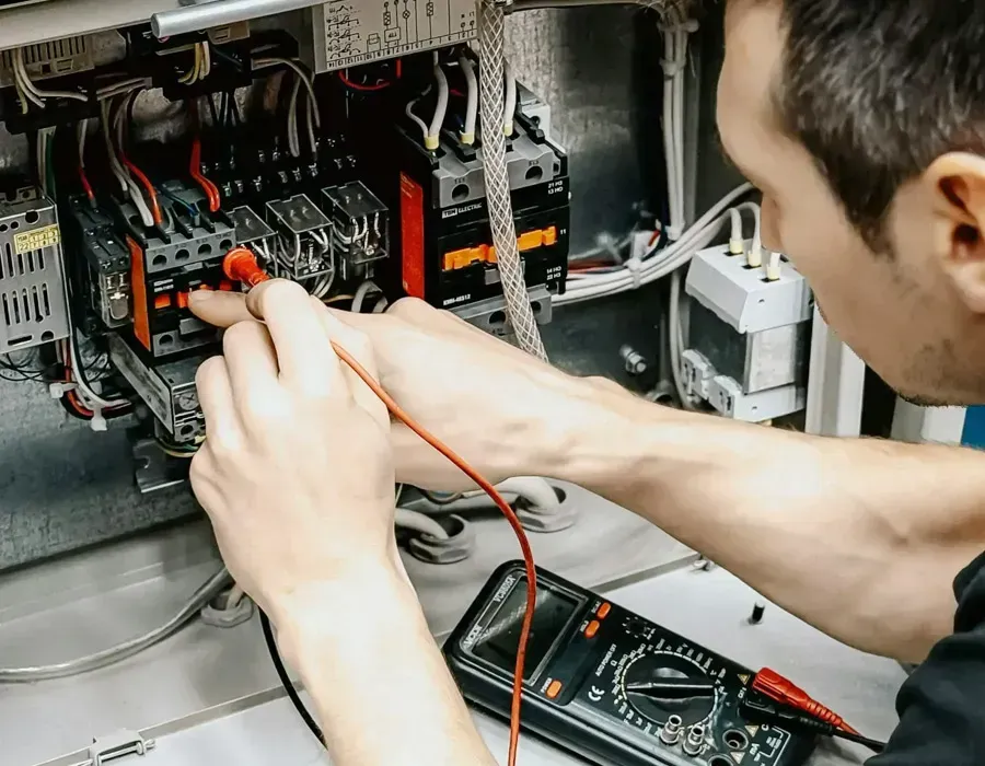 Technician wiring electronics inside an open computer/server cabinet with a multimeter nearby