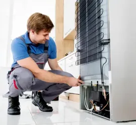 Technician kneeling beside a washing machine, using a tool to repair exposed wiring.