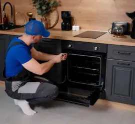 Person installing an oven in a modern kitchen with dark cabinets and wood countertops