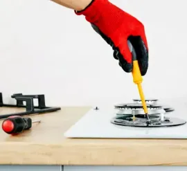 Hand holding yellow screwdriver tightening a gas stove burner on a kitchen counter