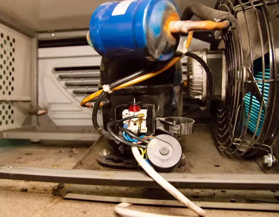 Blue compressor and fan inside a refrigeration unit, with wiring and pipes visible.