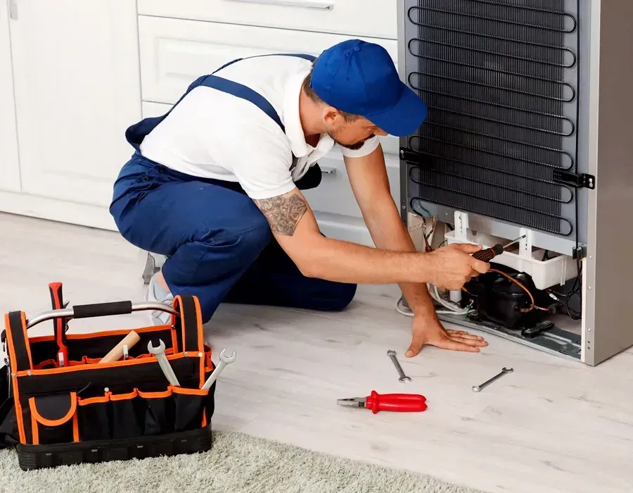 Technician repairing a refrigerator with tools beside him in a home kitchen