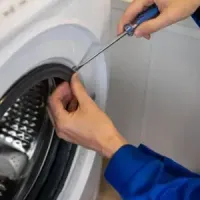 Person wiring an orange electrical component on a kitchen counter beside tools and a toolbox