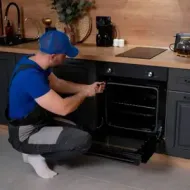 Person kneeling by an open oven, adjusting it in a modern kitchen