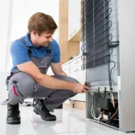 Technician crouching to repair wiring behind a white appliance in a bright room
