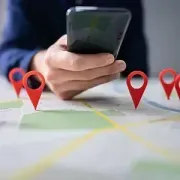 Hand holding a smartphone over a map with red location pins