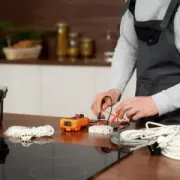 Person wiring an orange electrical component on a kitchen counter beside tools and a toolbox