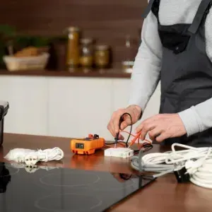 Person wiring an orange electrical component on a kitchen counter beside tools and a toolbox